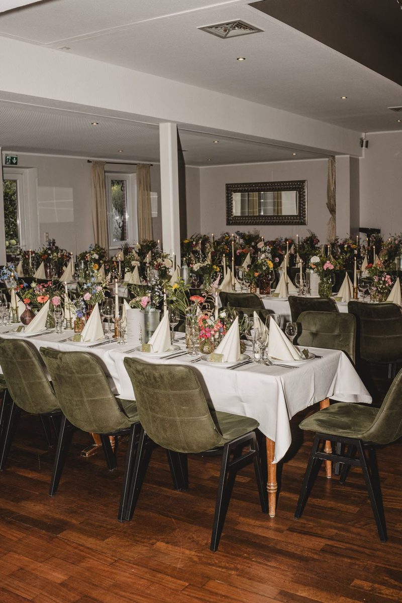 Heller Saal mit rund eingedeckten Tischen und Deckenventilator
